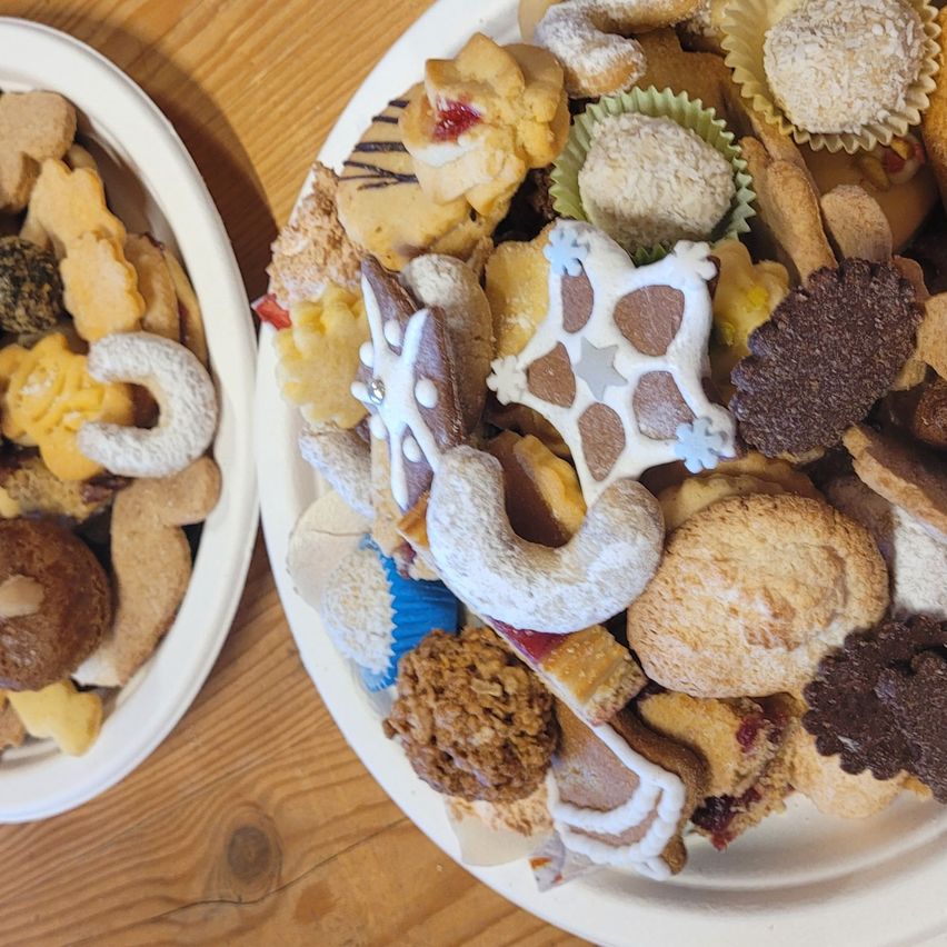 Zwei Teller mit verschiedenen Keksen, einer mit Halbmonden und der andere mit sternförmigen, Schokoladen- und verzierten Keksen, stehen auf einem Holztisch.