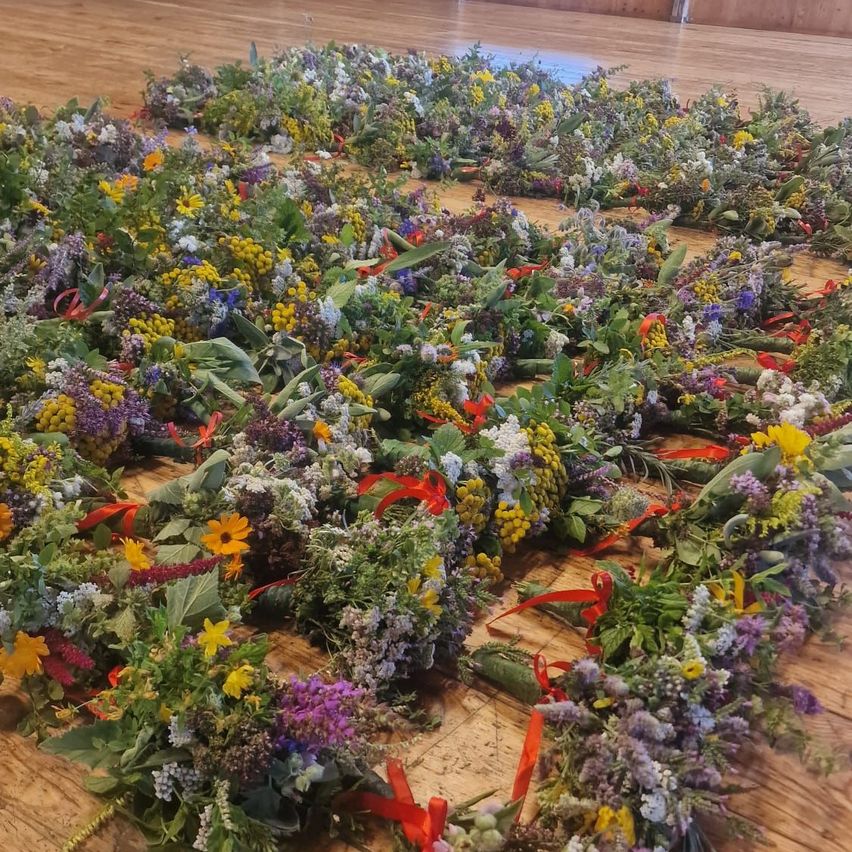 A circular arrangement of various flowers and greenery on a wooden floor, adorned with red ribbons.