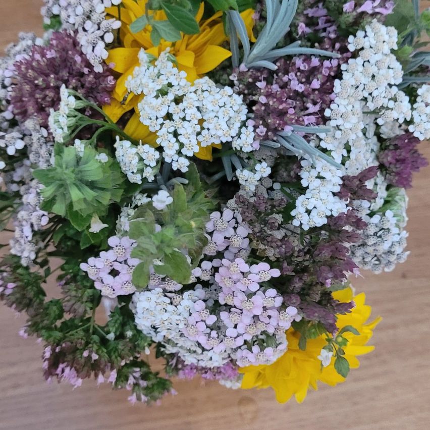 A close-up of a bouquet with various flowers, including white, purple, and yellow blooms, arranged on a wooden surface.