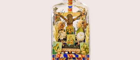 Eine durchsichtige Flasche enthält ein Miniaturkreuz und Blumendekorationen. Es gibt auch Bilder religiöser Figuren und Symbole.