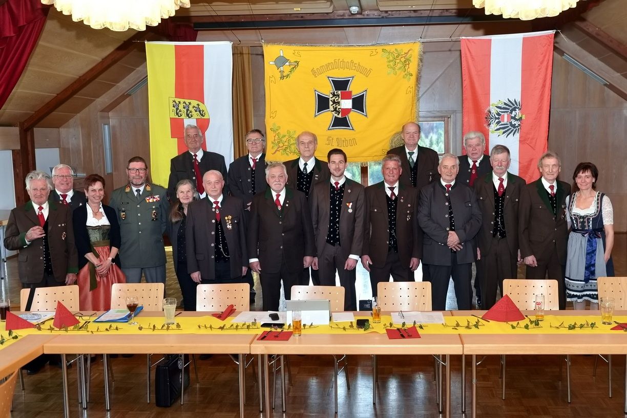 Eine Gruppe formell gekleideter Männer und Frauen posiert für ein Foto vor Tischen mit Fahnen in einem Raum.