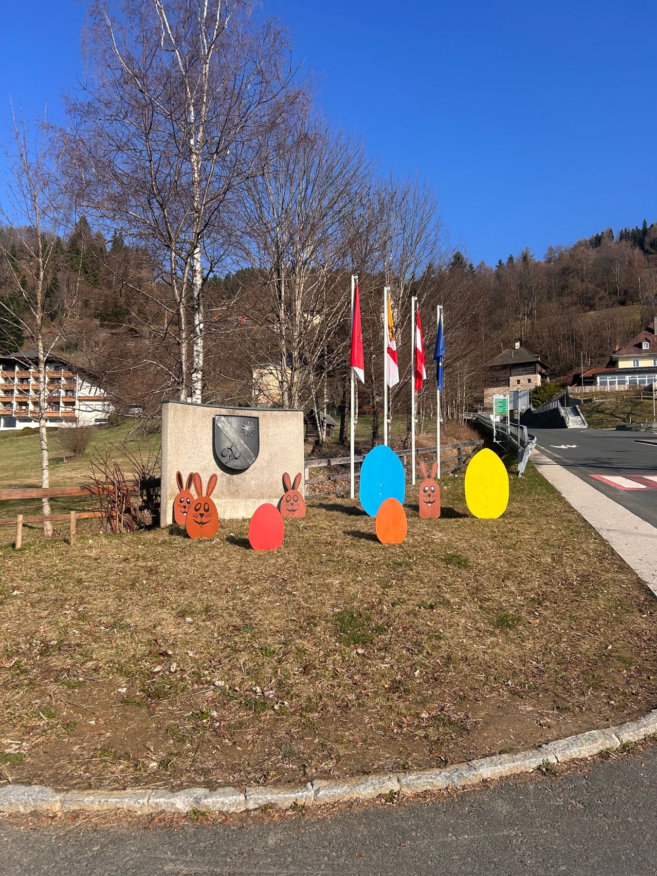 Eine Rasenfläche mit Osterhasenausschnitten und Flaggen, umgeben von Bäumen und einem kleinen Denkmalstein mit Design.