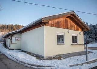 Ein kleines weißes Haus mit einem braunen Dach und Fenstern, gelegen in einer verschneiten Landschaft mit Bäumen im Hintergrund.