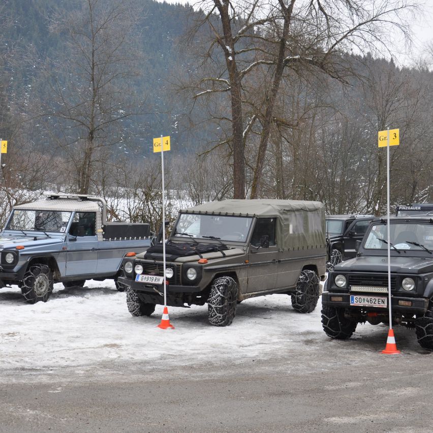 Mehrere Geländewagen sind in einem verschneiten Bereich geparkt. Die Fahrzeuge sind nummeriert und haben gelbe Schilder mit Nummern. Die Fahrzeuge sind in einer Reihe geparkt, mit einem Berg im Hintergrund.