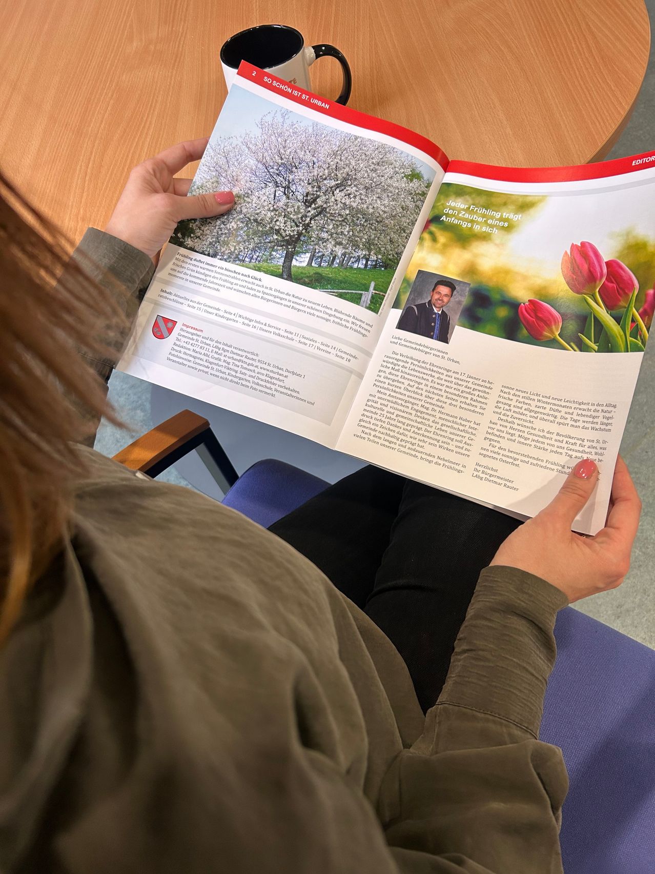 Eine Frau liest eine offene Zeitschrift mit einem Bild eines Mannes und Blumen auf der rechten Seite. Die linke Seite zeigt einen blühenden Baum.