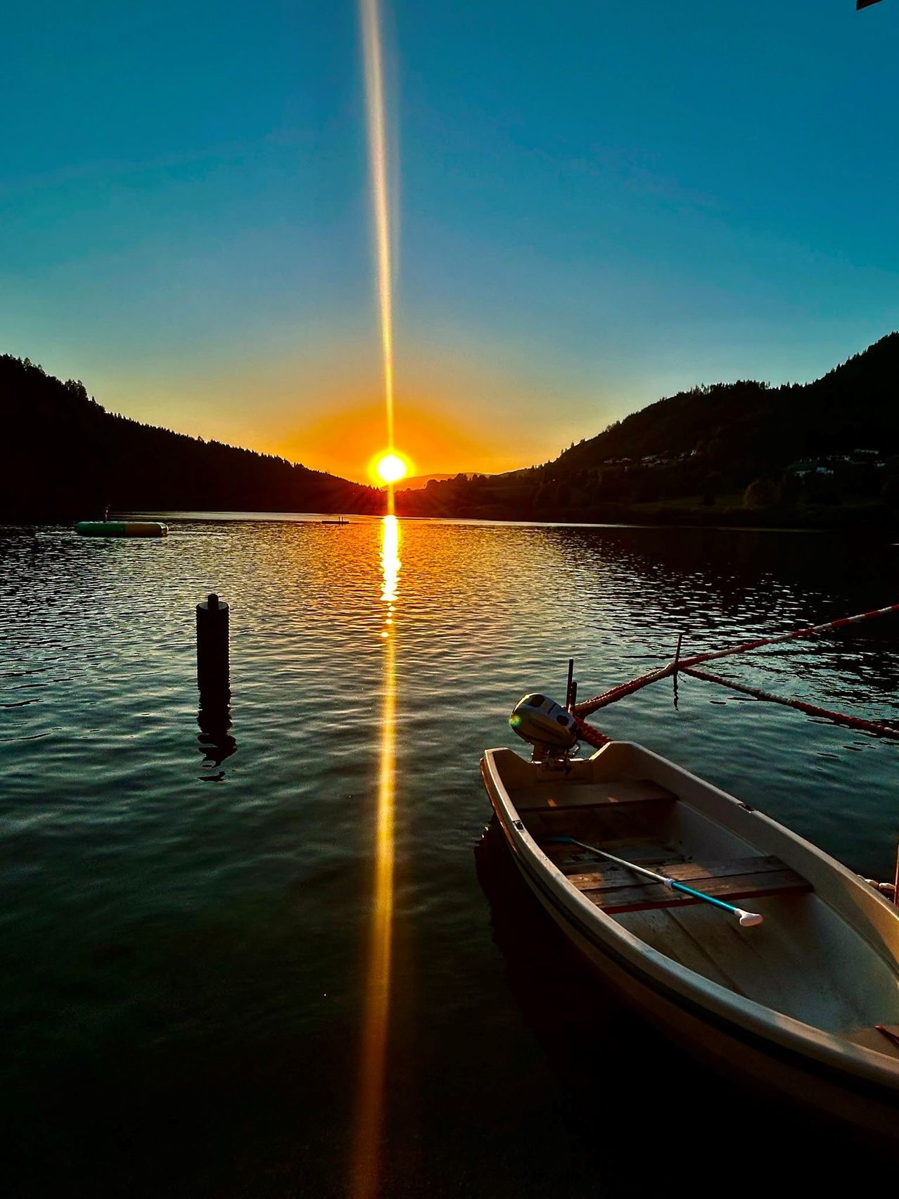 Ein ruhiger Sonnenuntergang über einem ruhigen See mit einem angedockten Boot an der Seite und einem schwimmenden Bojen in der Nähe.