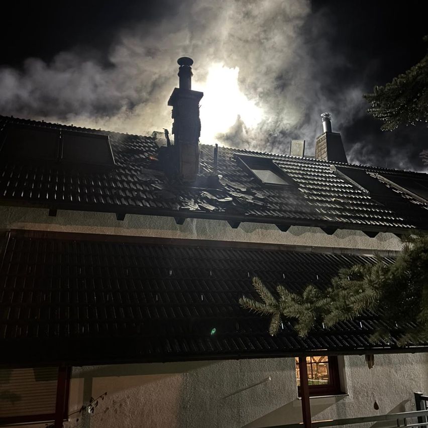 Ein nächtlicher Blick auf ein Haus, aus dessen Dach Rauch aufsteigt und ein helles Licht den Himmel erhellt.