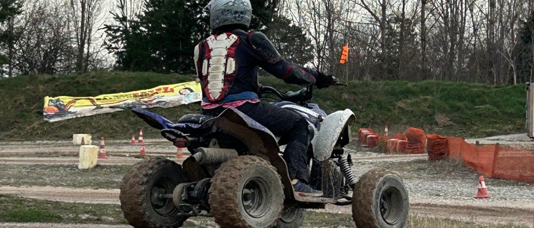 Eine Person fährt ein vierrädriges ATV auf einer Dirt-Strecke, mit orangefarbenen Kegeln und einem Banner im Hintergrund.