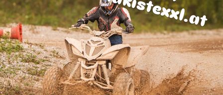 A person rides a four-wheeled ATV through mud on a dirt track. The rider wears a helmet and gloves. The image has a watermark with a URL.
