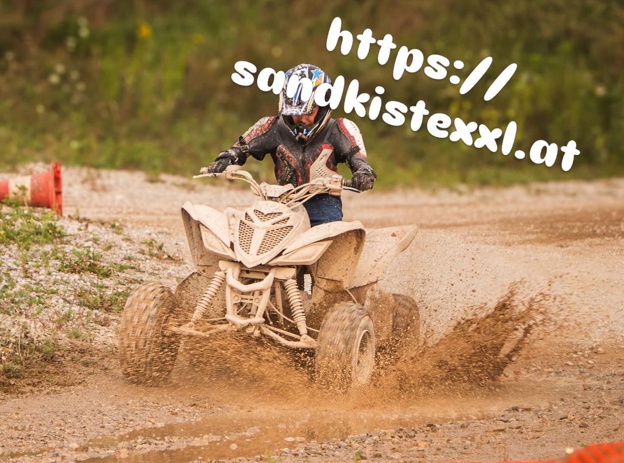 A person rides a four-wheeled ATV on a muddy trail, wearing a helmet and gloves. The image is slightly blurred.