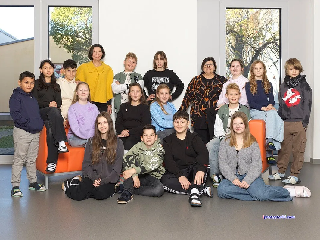 Eine Gruppe von Schülern und zwei Lehrern posiert für ein Foto in einem Klassenzimmer mit großen Fenstern.