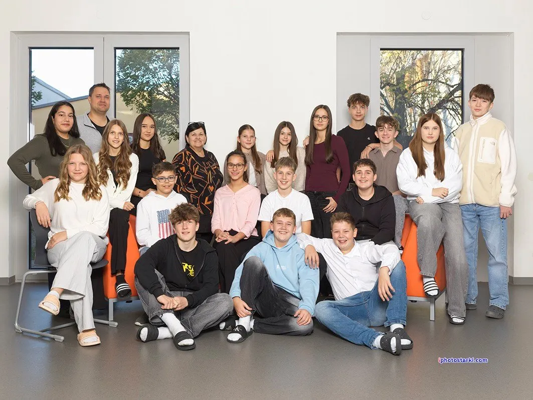 Eine Gruppe junger Menschen und Erwachsener posiert für ein Foto in einem Raum mit weißen Wänden, weißem Boden und Glasfenstern. Einige sitzen auf orangefarbenen Beanbags.
