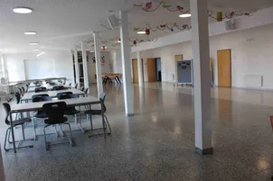 Ein leerer Raum mit Tischen und Stühlen, mit weißen Wänden und Böden, sowie Türen und einem Schreibtisch. Dekorationen hängen von der Decke.