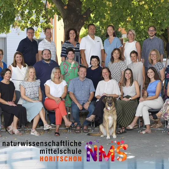 Ein Gruppenfoto von Menschen, einschließlich Erwachsener und eines Hundes, die unter einem Baum sitzen. Sie sind wahrscheinlich Mitarbeiter oder Fakultätsmitglieder einer Schule. Der Name der Schule ist Horitschon.