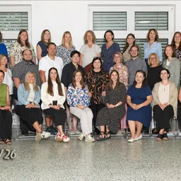 Eine Gruppe von Menschen, sowohl Männer als auch Frauen, sitzen und stehen in einem Raum, wahrscheinlich für ein Gruppenfoto. Sie sind in verschiedenen Outfits gekleidet.