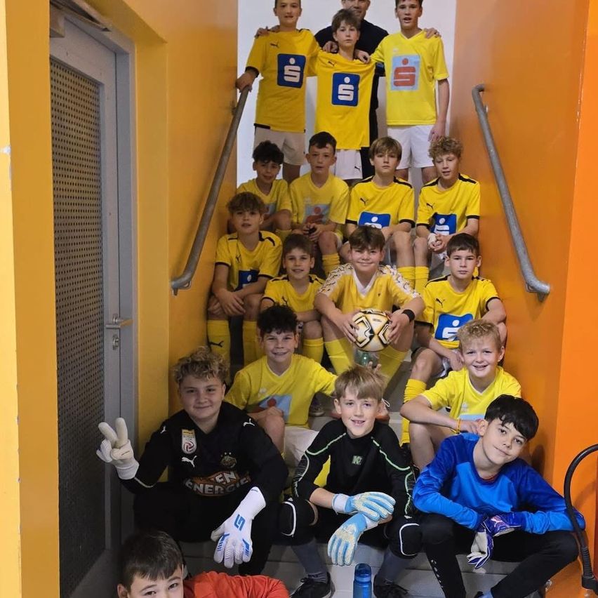 Eine Gruppe junger Fußballspieler in gelben Trikots posiert auf den Stufen, einer hält einen Fußball.