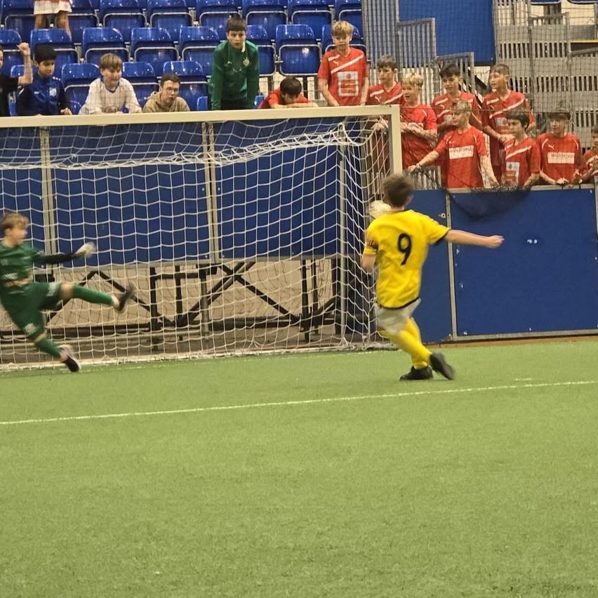 Zwei Fußballspieler, einer in Grün und der andere in Gelb, spielen ein Match, während eine Menge auf den Tribünen zuschaut.