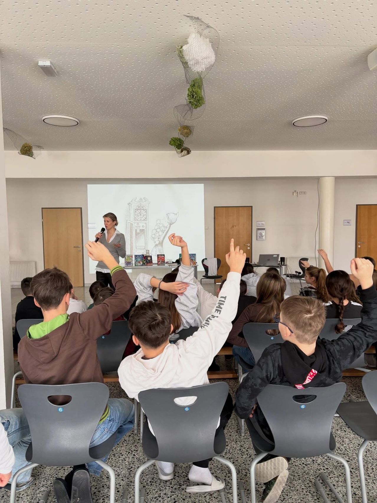Eine Frau hält eine Präsentation für eine Klasse von Schülern ab, die ihre Hände heben und aufmerksam zuhören.