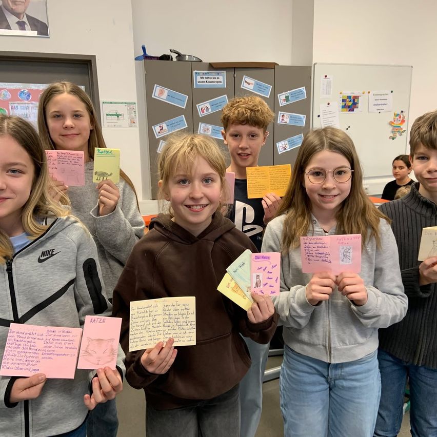 Eine Gruppe von Kindern in einem Klassenzimmer, die bunte Notizen hochhalten und lächeln, mit einer Tafel und einem Bulletin Board im Hintergrund.