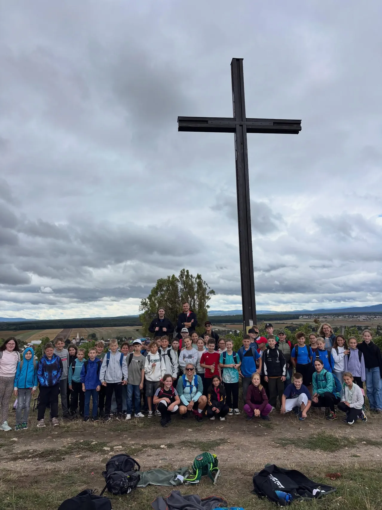 Eine Gruppe von Kindern und Erwachsenen posiert für ein Foto vor einem großen Kreuz auf einem Hügel.