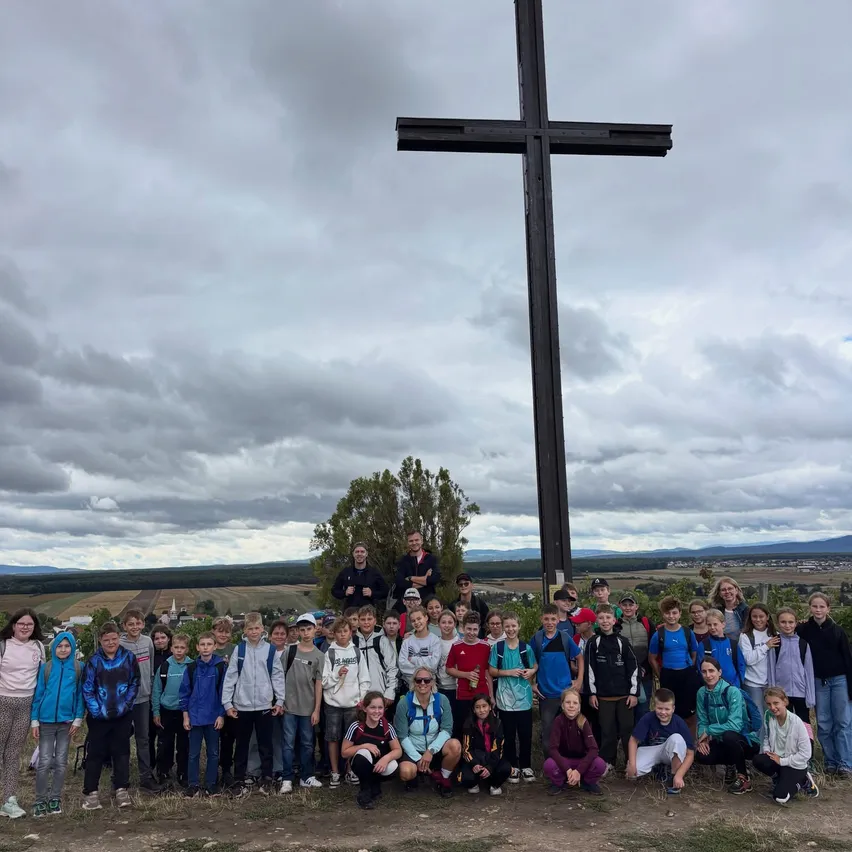 Eine Gruppe von Kindern und Erwachsenen posiert für ein Foto vor einem großen Kreuz auf einem Hügel.