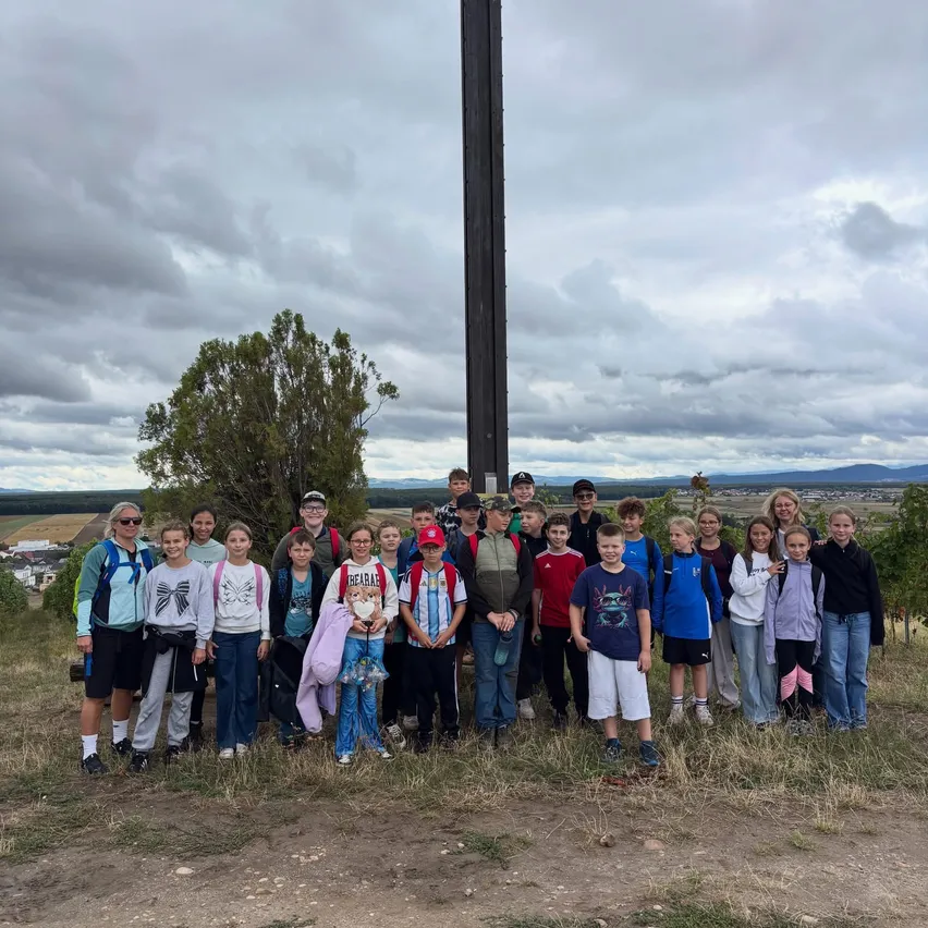 Eine Gruppe von Menschen posiert für ein Foto vor einem hohen Kreuz auf einem Hügel.