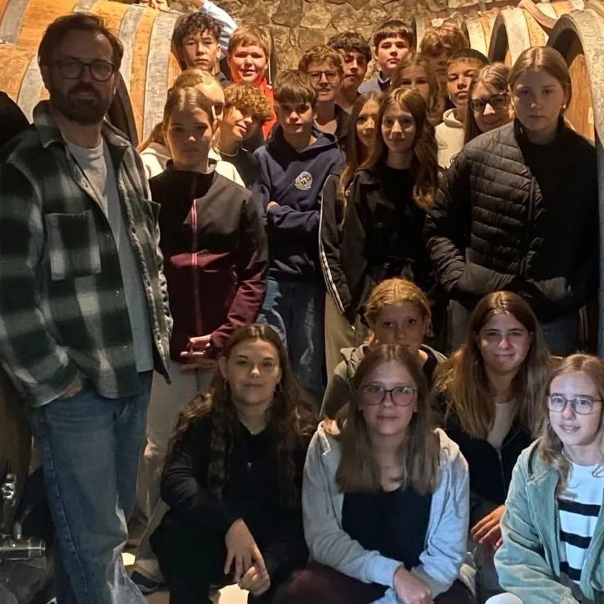 Eine Gruppe von Menschen, darunter junge Erwachsene und ein Mann, posiert für ein Foto in einem Raum mit Holzfässern.