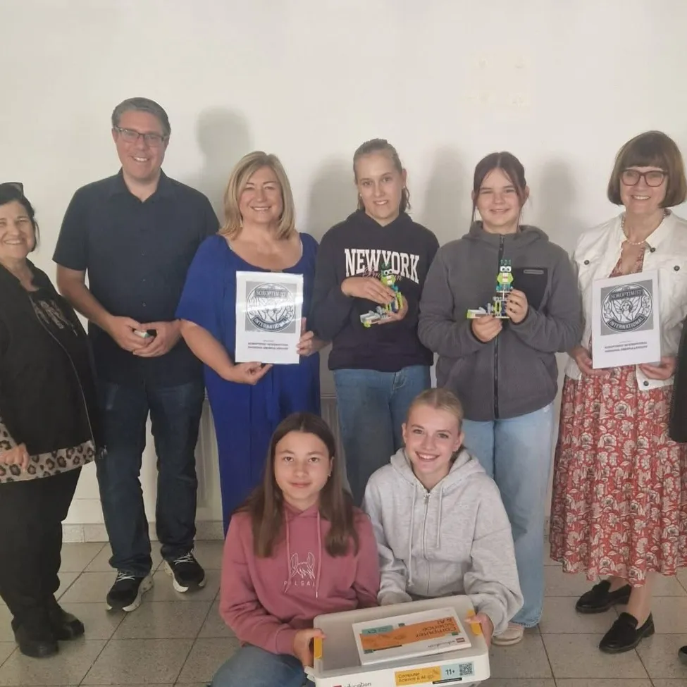 Eine Gruppe von Menschen posiert für ein Foto in einem Raum. Sie alle lächeln und halten Urkunden und Schachteln.