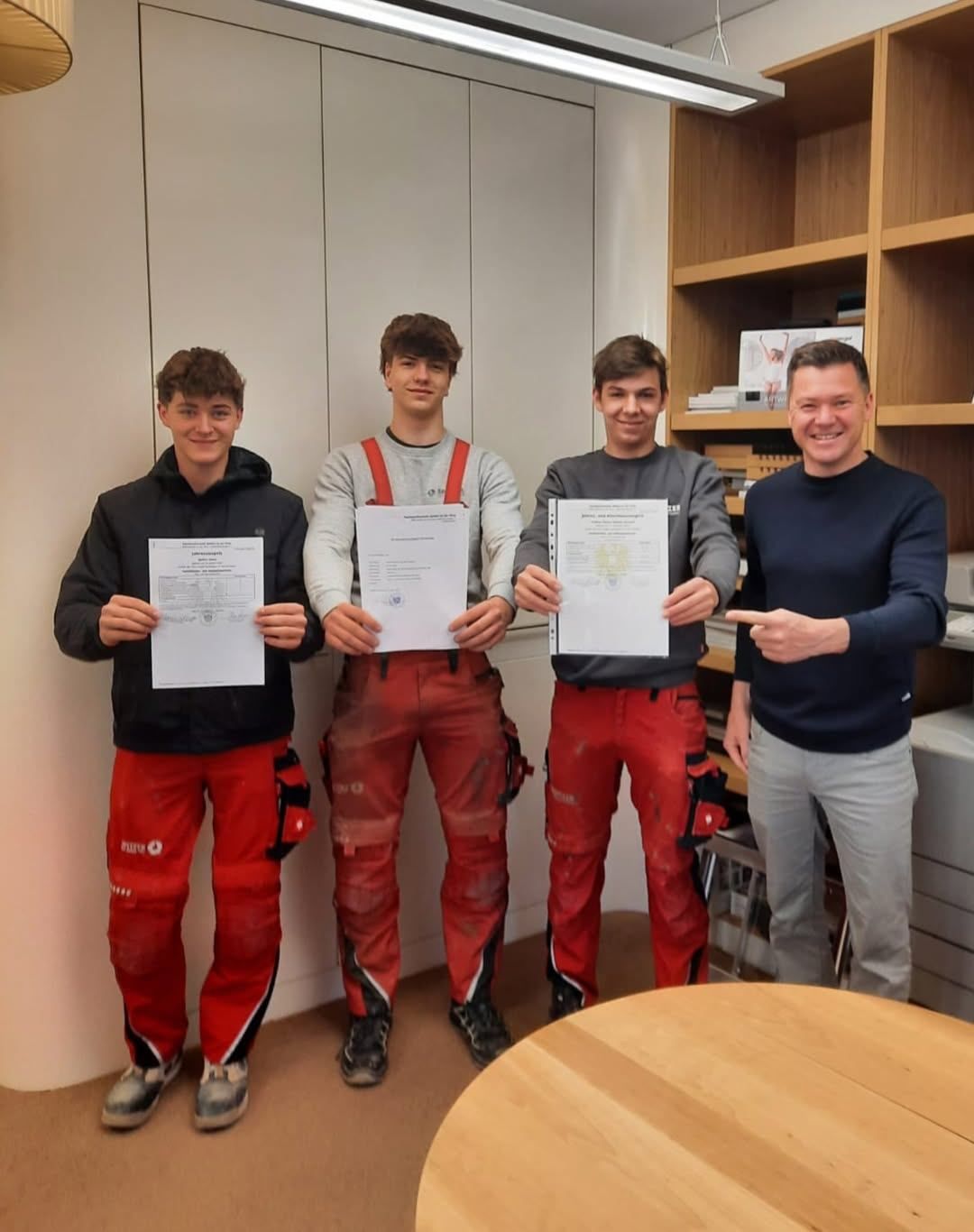 Vier Männer in einem Raum. Drei von ihnen halten Papiere und ein Mann zeigt auf sie.