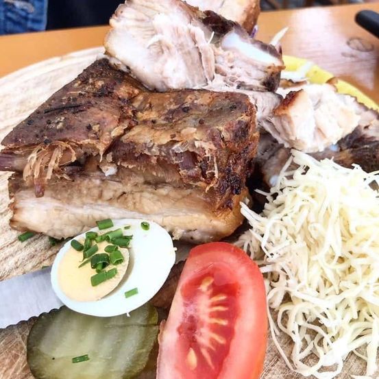 Ein Holzteller mit einem Gericht aus gebratenem Fleisch, einem hart gekochten Ei mit Frühlingszwiebeln, einer Tomatenscheibe und geriebenem Käse.