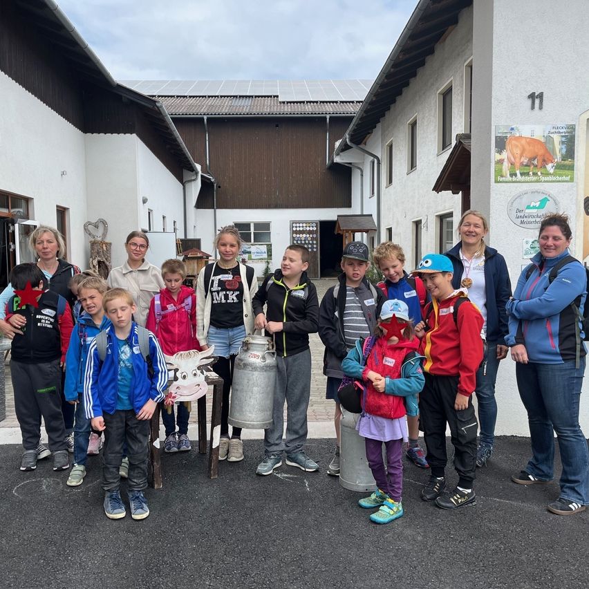Eine Gruppe von Kindern und Erwachsenen steht vor einem Gebäude mit Solarpanelen auf dem Dach. Sie posieren für ein Foto mit einigen Eimern und einer Kuhdekoration.
