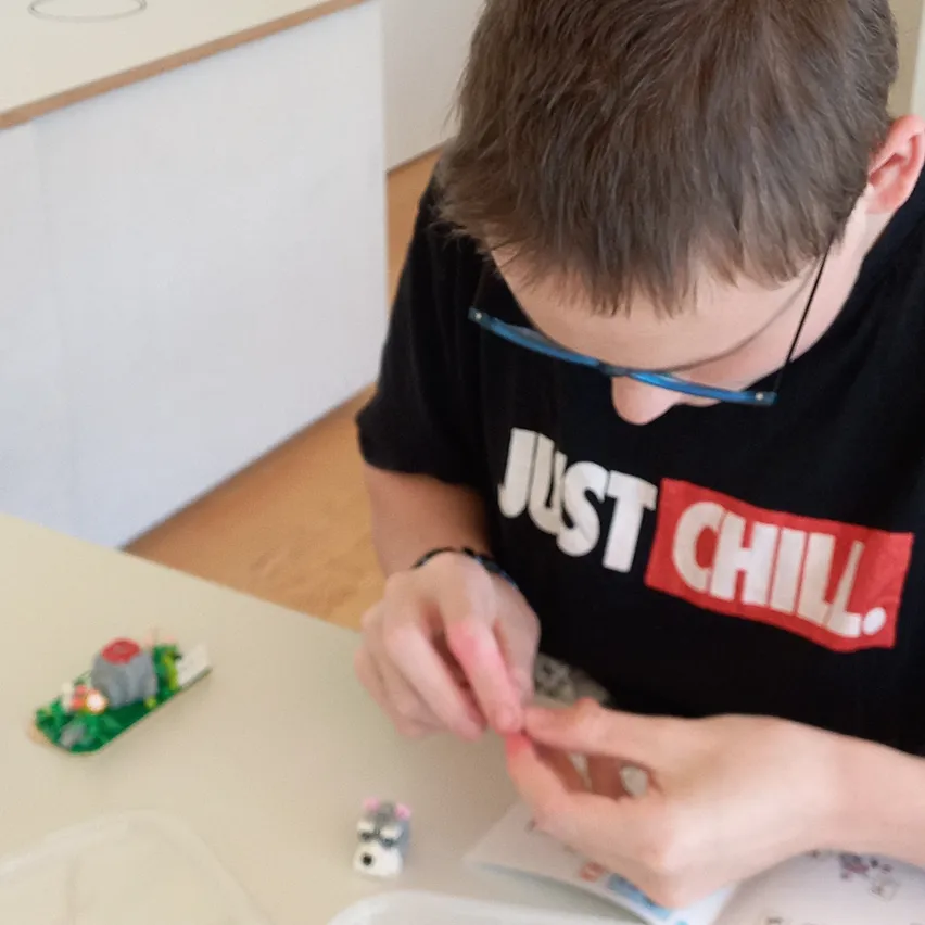Ein Junge mit Brille und einem schwarzen T-Shirt mit 'Just Chill' Aufdruck arbeitet an einem kleinen elektronischen Projekt auf einem Tisch.