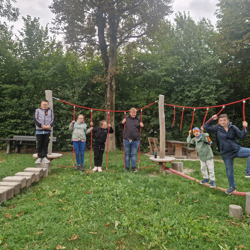 Eine Gruppe von Kindern und Erwachsenen spielt auf einer Seilschaukel in einem Park.