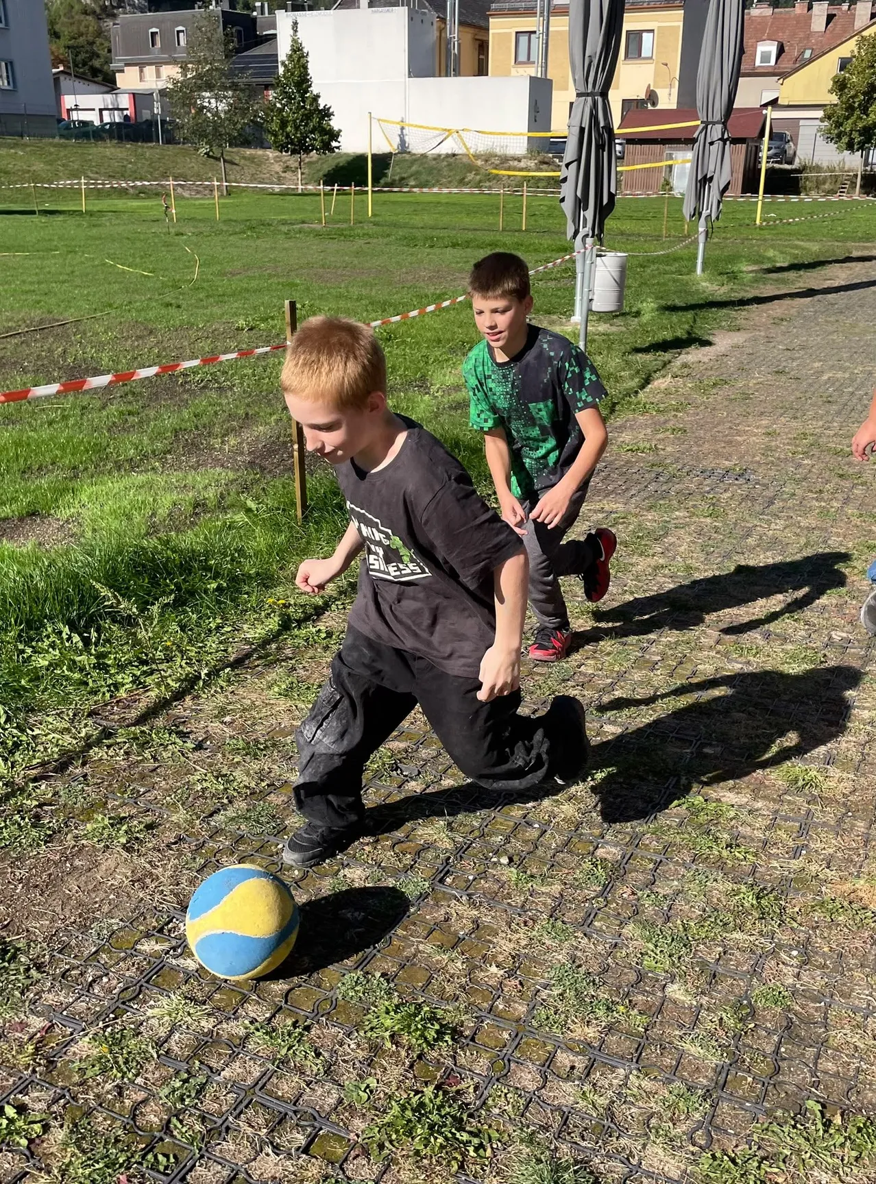 Zwei Jungen spielen Fußball auf einem Erdfeld mit einem gelben und blauen Ball.