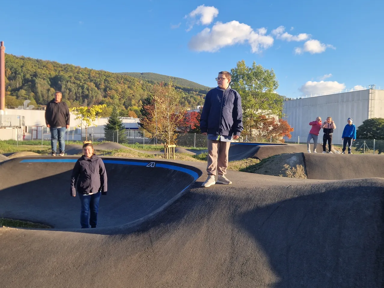 Eine Gruppe von Menschen steht an einem Skatepark an einem sonnigen Tag.