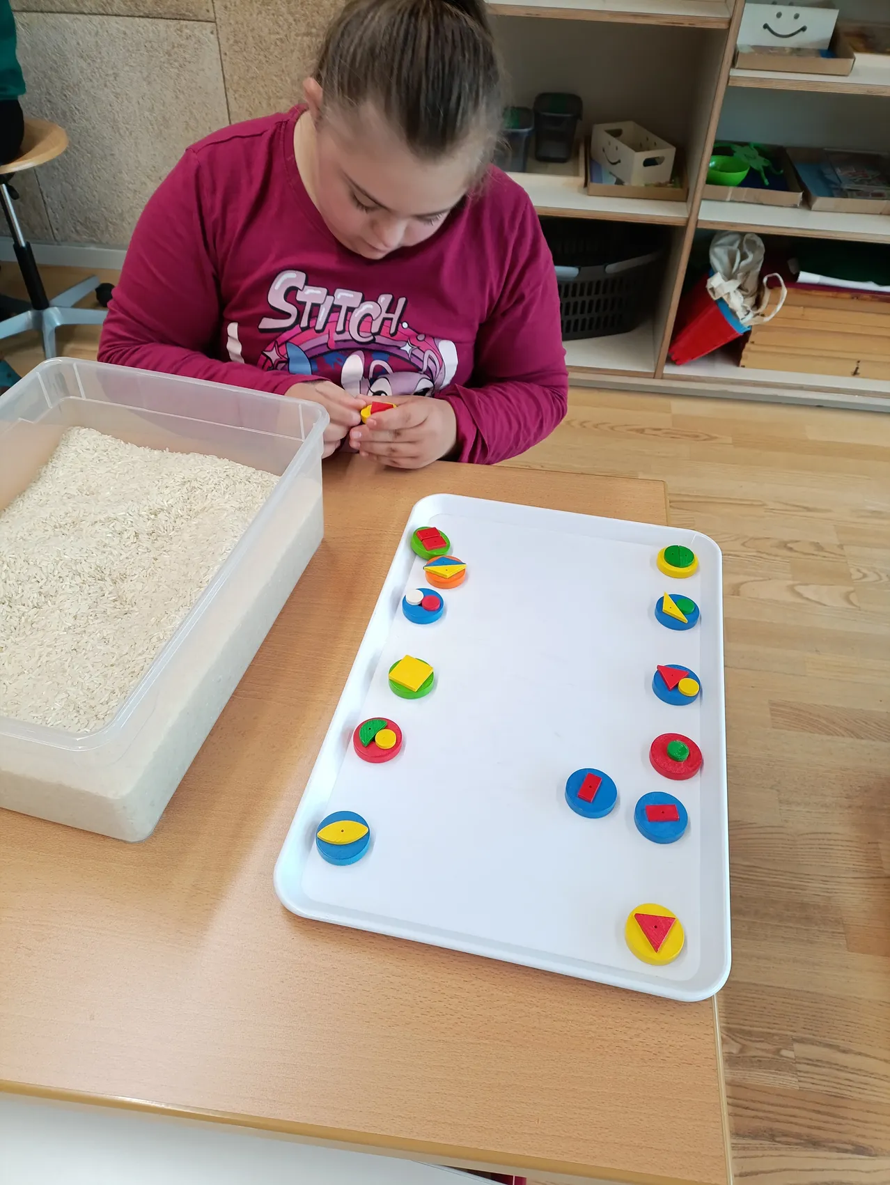 Ein junges Mädchen sitzt an einem Tisch und ist mit farbenfrohen geometrischen Formen beschäftigt.