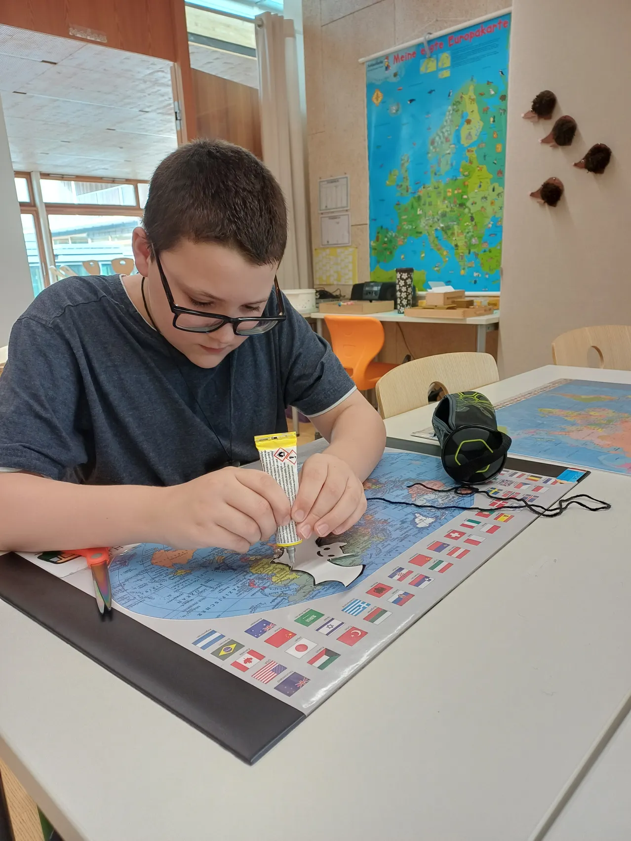 Ein Junge mit Brille arbeitet an einer Karte mit Flaggen verschiedener Länder.