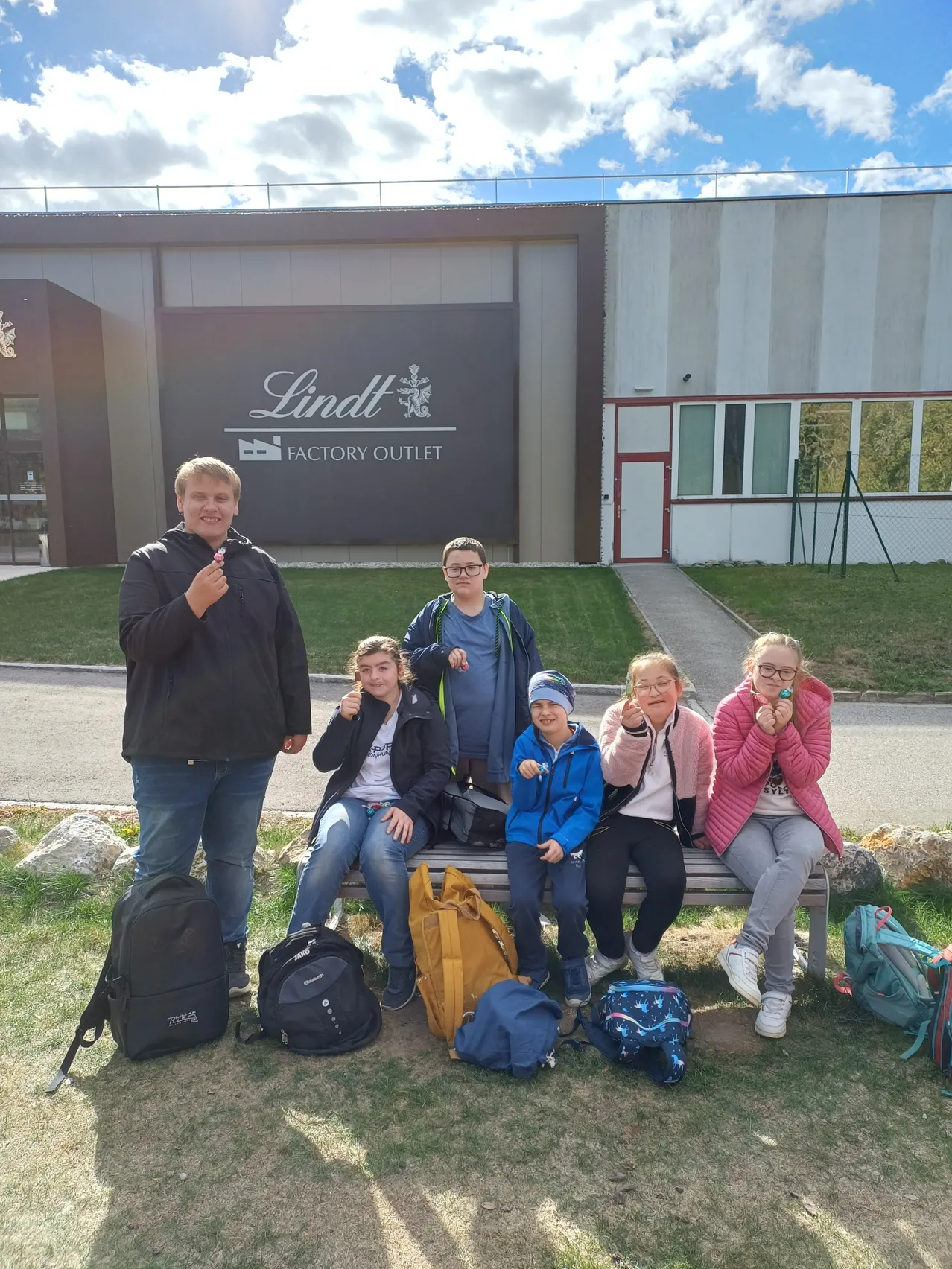 Eine Gruppe von Menschen posiert für ein Foto vor einem Gebäude mit dem Schild 'Lindt Factory Outlet'.