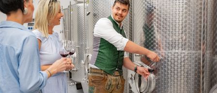 Ein Mann schenkt Wein in Gläser für eine Gruppe von Menschen in einem Weinkeller ein.