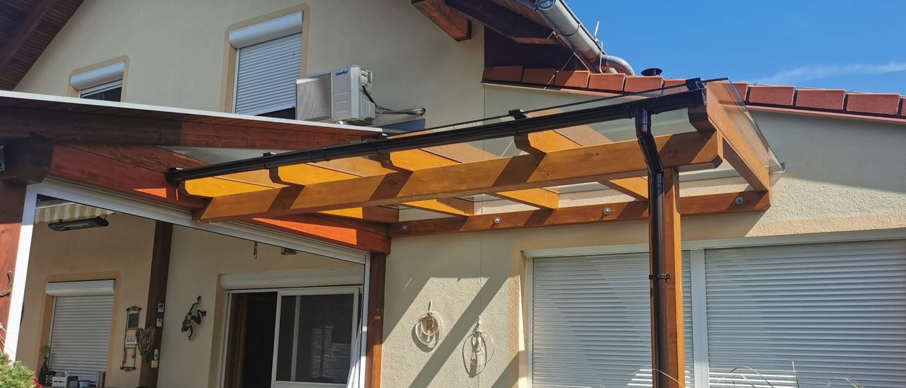 Ein Patio mit einer hölzernen Pergola, die an ein Haus angebaut ist. Ein Whirlpool steht unter der Pergola, und ein Hund liegt auf dem Boden.