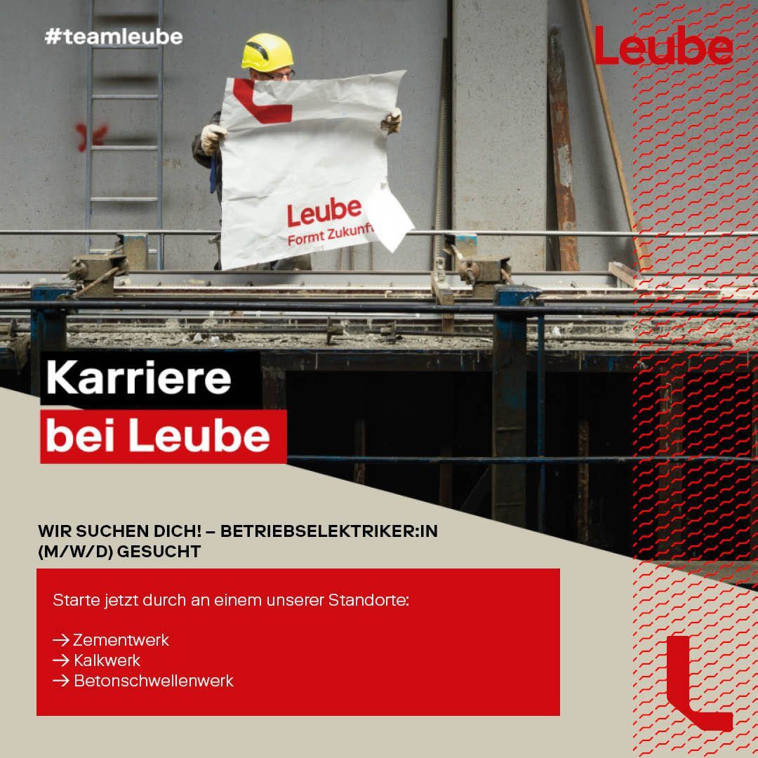 Ein Bauarbeiter in einem Zementwerk hält ein Schild mit der Aufschrift 'Leube'. Das Schild hat einen roten Rand und ist weiß geschrieben. Der Arbeiter trägt einen gelben Helm.