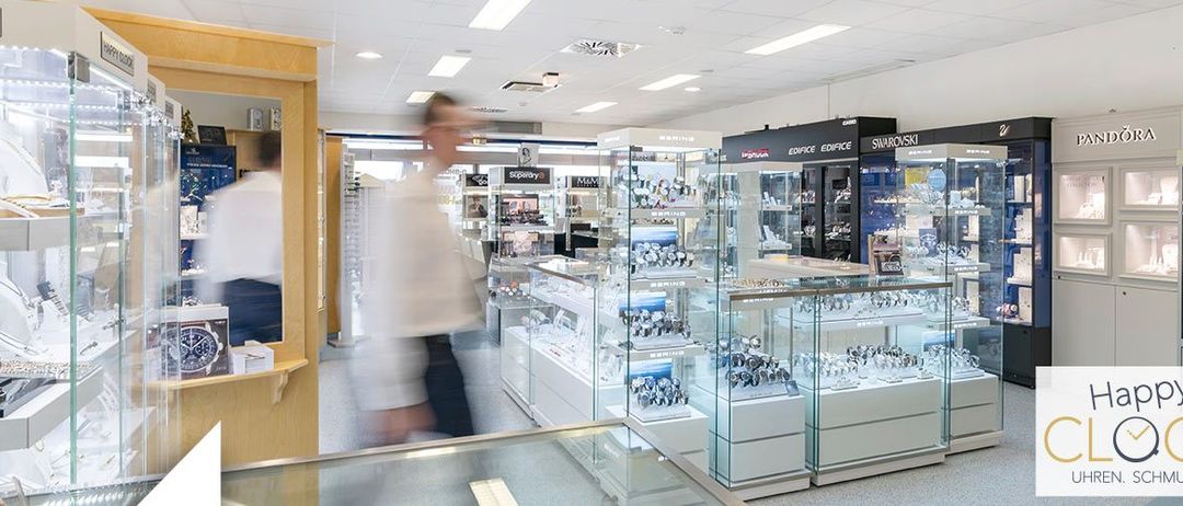 Ein Bild eines Juwelierladens mit mehreren Personen, die an den Displays vorbeigehen. Der Laden hat Glasvitrinen und Regale, die mit Schmuck gefüllt sind.