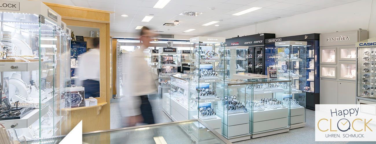 Ein Bild eines Juwelierladens mit mehreren Personen, die an den Displays vorbeigehen. Der Laden hat Glasvitrinen und Regale, die mit Schmuck gefüllt sind.