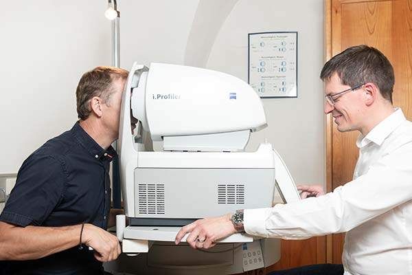 Ein Mann mit einem Lächeln lässt sich von einem Arzt die Augen mit einem i.Profiler-Gerät überprüfen.