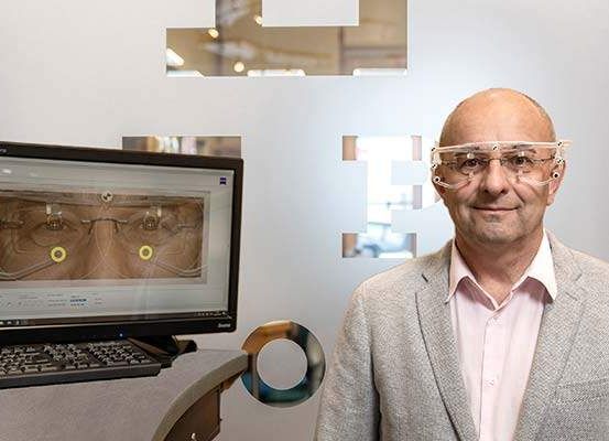 Ein Mann mit Brille steht vor einem Computerbildschirm und einer Wand mit einem F-Logo.