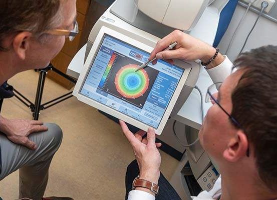 Zwei Männer untersuchen ein Tablet, das einen farbigen Kreis mit Daten und einem Stift anzeigt. Ein Mann trägt eine Brille und eine Armbanduhr, der andere eine Uhr.