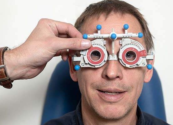 Ein Mann trägt ein Augenuntersuchungsgerät mit roten und blauen Linsen und lächelt, während er in einem blauen Stuhl sitzt.