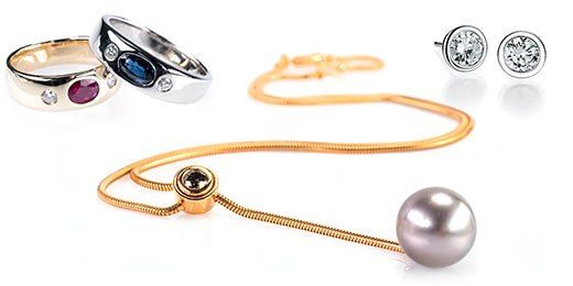 Verschiedene Schmuckstücke sind auf weißem Hintergrund zu sehen. Dazu gehören ein Ring, eine Halskette und Ohrringe. Die Halskette hat einen großen Perlenanhänger.