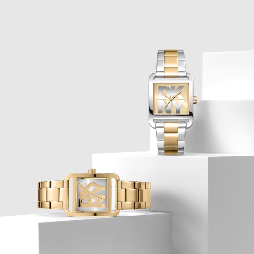 Zwei DKNY Uhren, eine in Gold und eine in Silber, auf weißen Oberflächen ausgestellt.