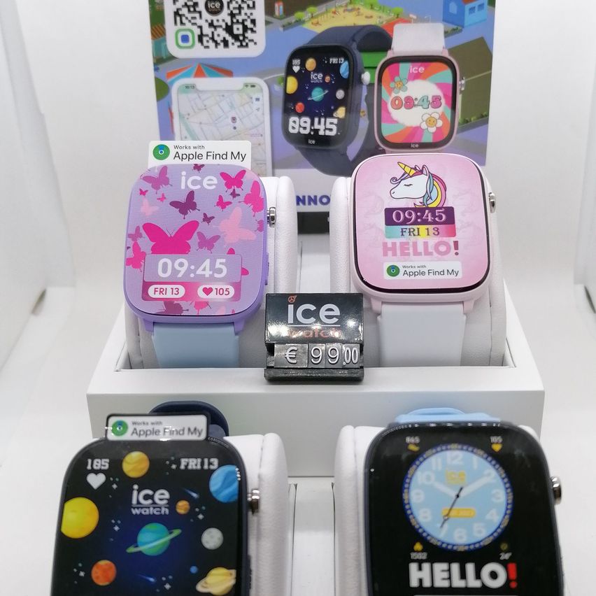 Eine Ausstellung von vier Smartwatches in einer Box. Eine hat ein Einhorngesicht, eine hat Schmetterlinge, eine hat ein Planetenthema und eine sagt 'HALLO!'. Alle haben Apple Find My Aufkleber.